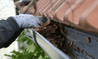 Commercial-gutter-cleaning-worker Hand picking leaves out and cleaning gutter.