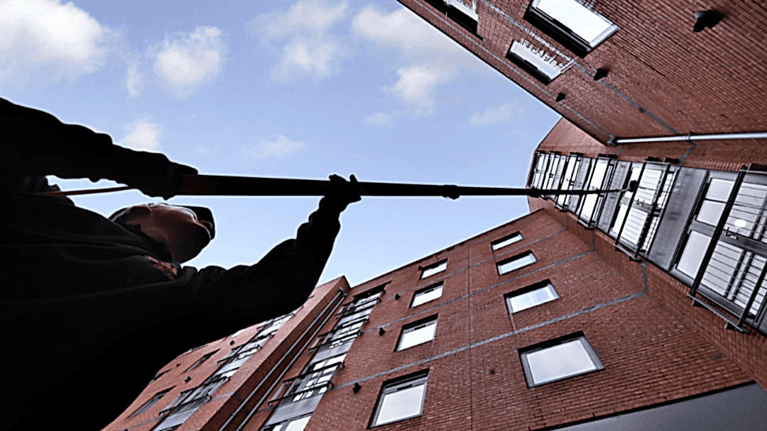 Commercial window cleaner using a water-fed pole to clean windows on high-rise building.